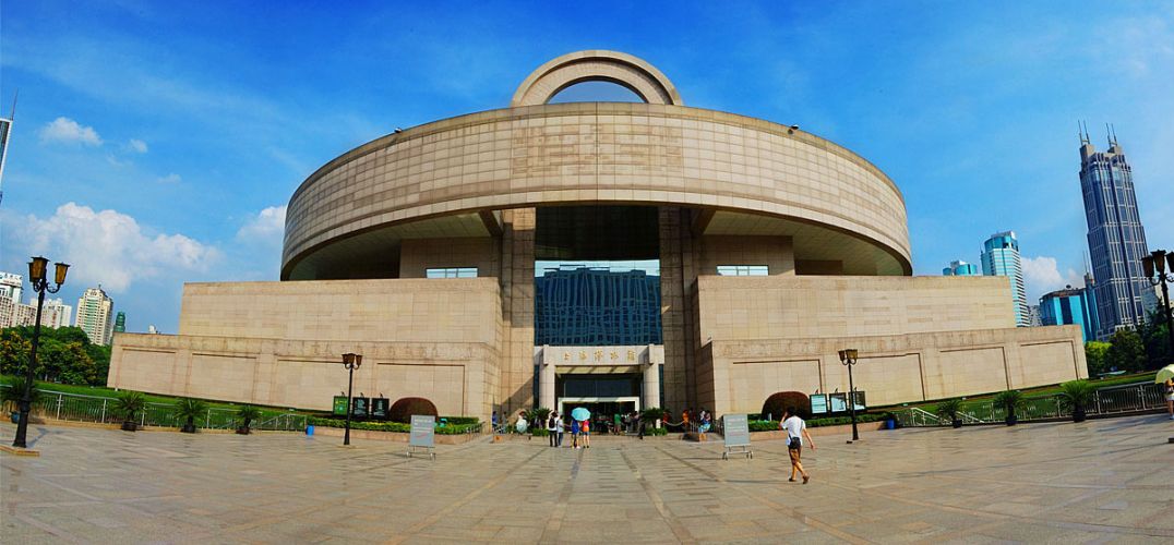 这是一张现代城市中的博物馆建筑照片，建筑呈半圆形，前方有宽阔的广场，几位行人在此散步。